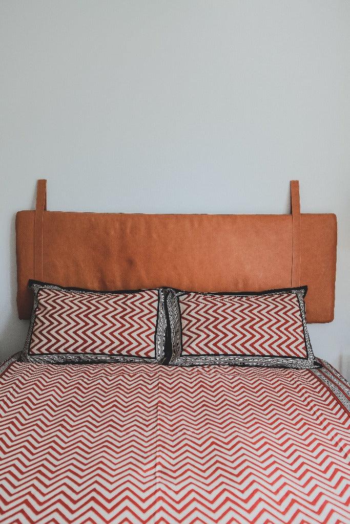 Queen bedding set in red zig zag pattern displayed on a modern bed with a leather headboard in a minimal room with white walls.