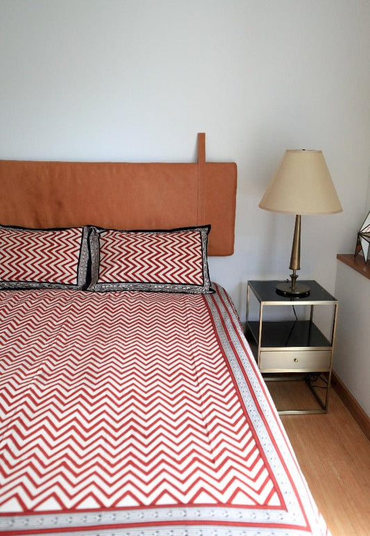 Queen bedding set in red zig zag pattern displayed on a modern bed with a leather headboard in a minimal room with white walls.